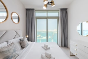 Ein Hotelzimmer mit einem großen Bett, zwei Nachttischen, einer Kommode und Blick auf ein Gewässer durch große Fenster.