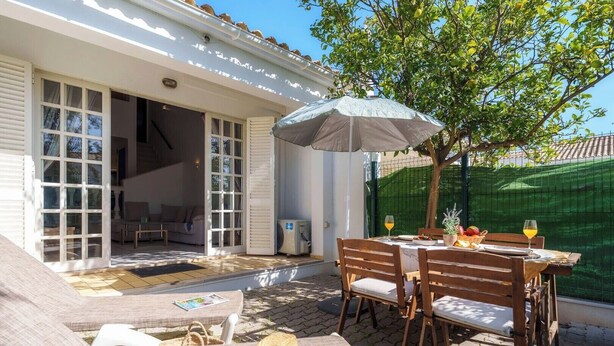 Een terras met een tafel voor twee personen, een overdekte zithoek en een overdekt buitenruimte met uitzicht op het huis.