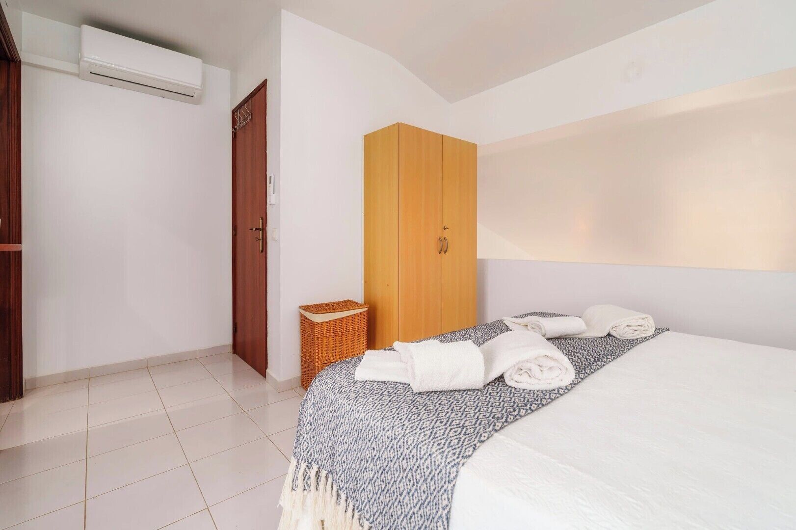 Ein Schlafzimmer mit Bett, Kleiderschrank, Korbwäscheschrank und Wandklimaanlage.