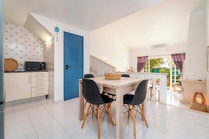 A modern kitchen with a blue door, white cabinets, and a dining area with a wooden table and black chairs. - Cosy 2bedroom townhouse 10mns from Olhos de Agua (Albufeira)