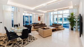 A modern living room with a glass dining table, sofas, and a flat-screen TV. - 4BR Palm Penthouse: Private Pool & Beach Access (Dubai)