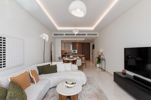 Ein modernes Wohnzimmer mit einer Eckcouch, einem Fernseher und einem Essbereich im Hintergrund.