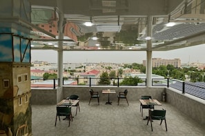 A rooftop terrace with tables and chairs, a city view, and solar panels. - Safia Plaza Hotel (Bukhara)