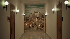 A hallway with a mural of a cityscape, two doors, and wall-mounted lights. - Safia Plaza Hotel (Bukhara)