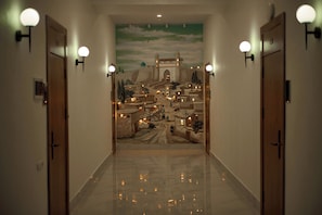 A hallway with a mural of a cityscape, two doors, and wall-mounted lights. - Safia Plaza Hotel (Bukhara)
