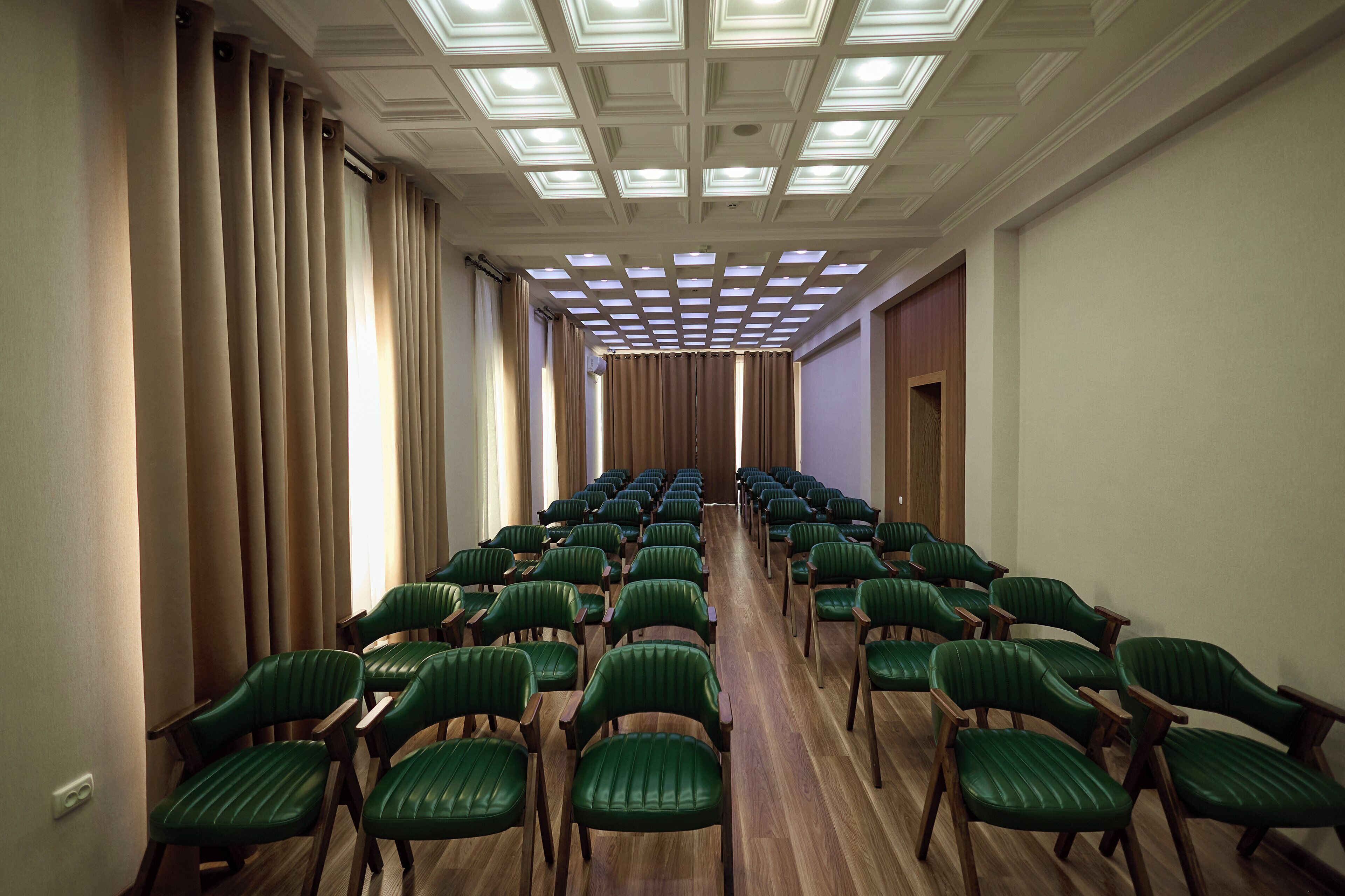 Una sala conferenze con file di sedie verdi, pavimento in legno e un soffitto con illuminazione a incasso.