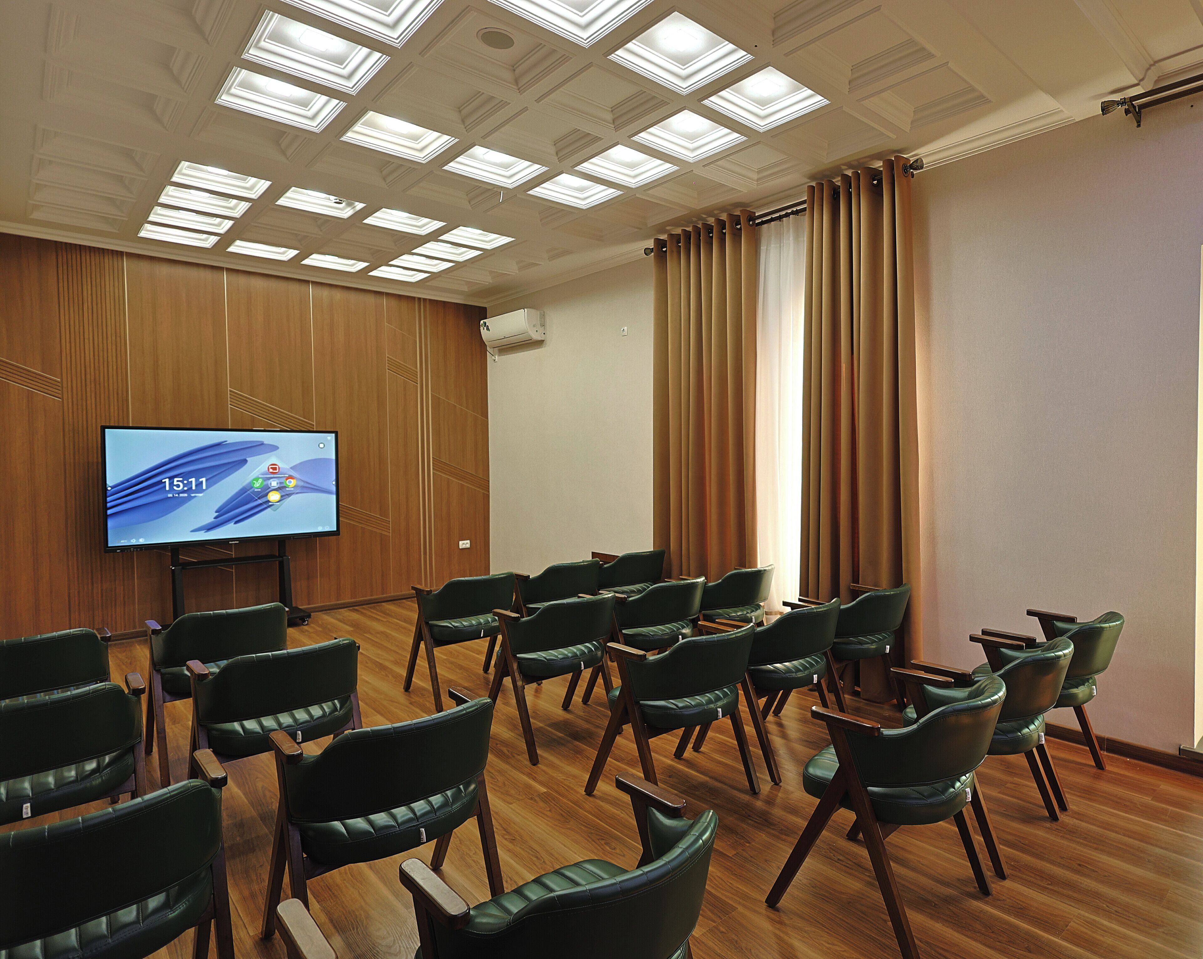 A conference room with a large screen, wooden panel walls, and rows of green chairs.
