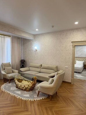 Een woonkamer met een beige bank, een glazen salontafel, een tapijtbegroeiing en een houten vloer.