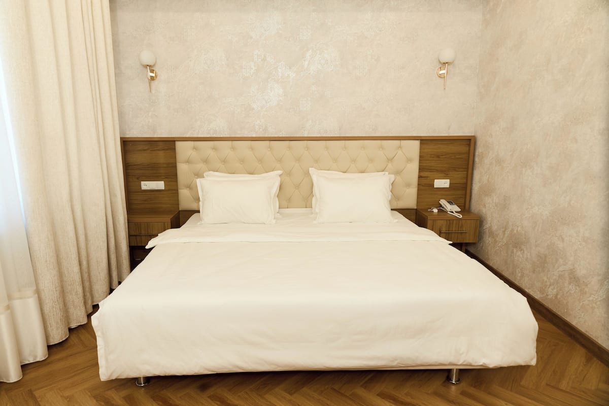 A neatly made bed with a wooden headboard, two bedside tables, and a wall-mounted telephone.