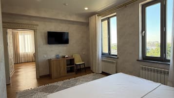 Ein Schlafzimmer mit Bett, Schreibtisch, Stuhl, Fernseher und großen Fenstern.
