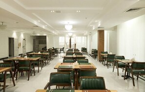 A spacious hotel dining area with multiple tables and chairs, a chandelier, and a large window. - Safia Plaza Hotel (Bukhara)