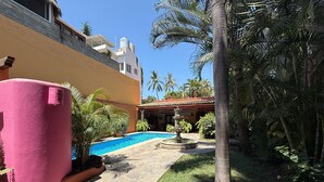 A pool area with a stone pathway, palm trees, and a building with a tiled roof. - Casa Sorpresa mexican charm by the beach (Sayulita)