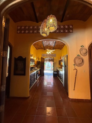 Un couloir avec un ventilateur de plafond, un mur décoré de motifs et une porte donnant sur un espace cuisine.