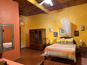 Une chambre avec un lit, une armoire, un miroir et un ventilateur de plafond.