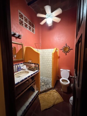Een badkamer met douche, toilet, wastafel en een plafondventilator.