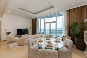 Ein modernes Wohnzimmer mit einem Glastisch, bequemen Sitzgelegenheiten, einem Flachbildfernseher und einem großen Fenster mit Blick auf die Stadt.