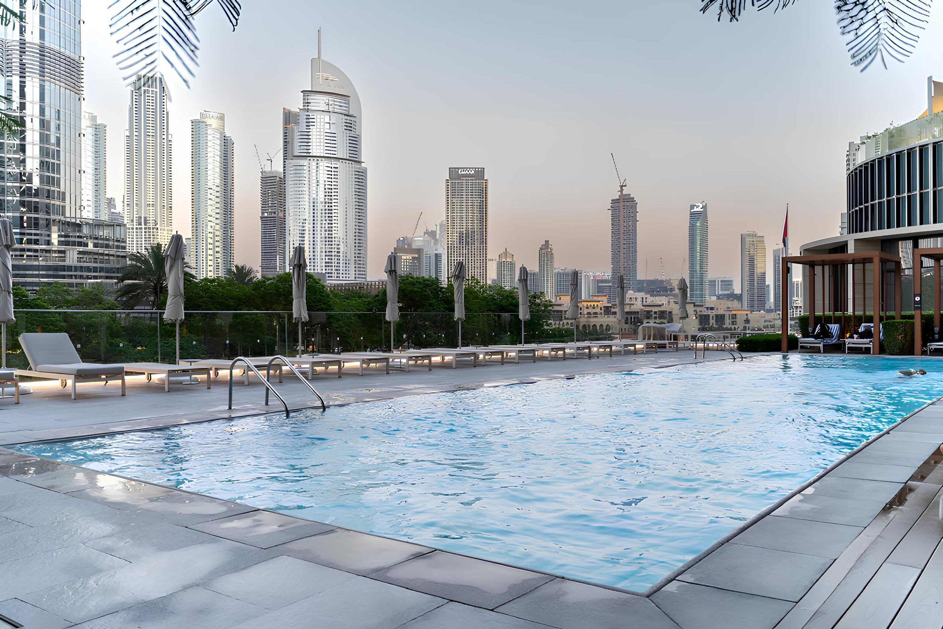 A rooftop pool with a city skyline view, lounge chairs, and a modern building with a dome structure.