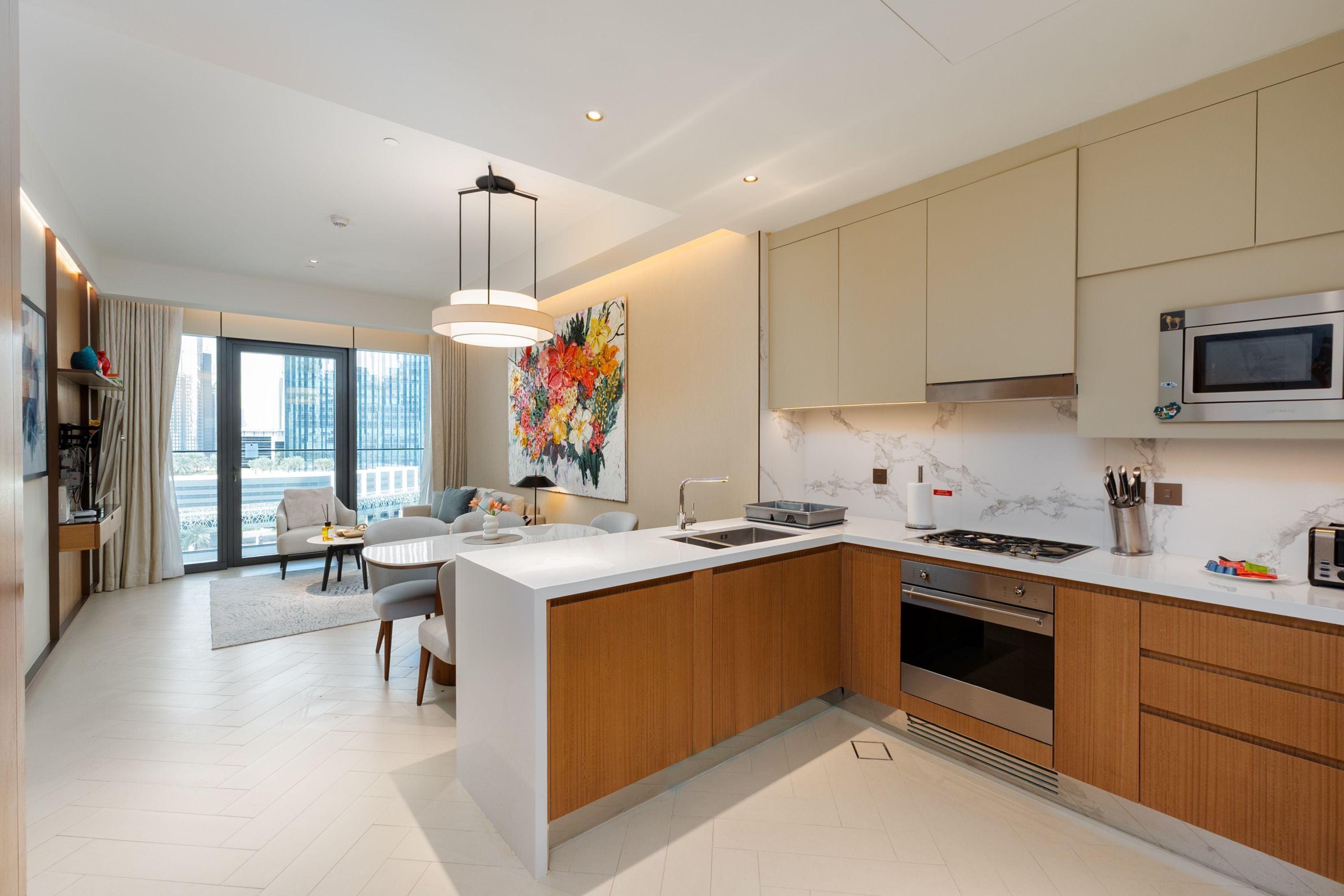 A modern kitchen with a central island, built-in oven, microwave, and a large window offering a city view.