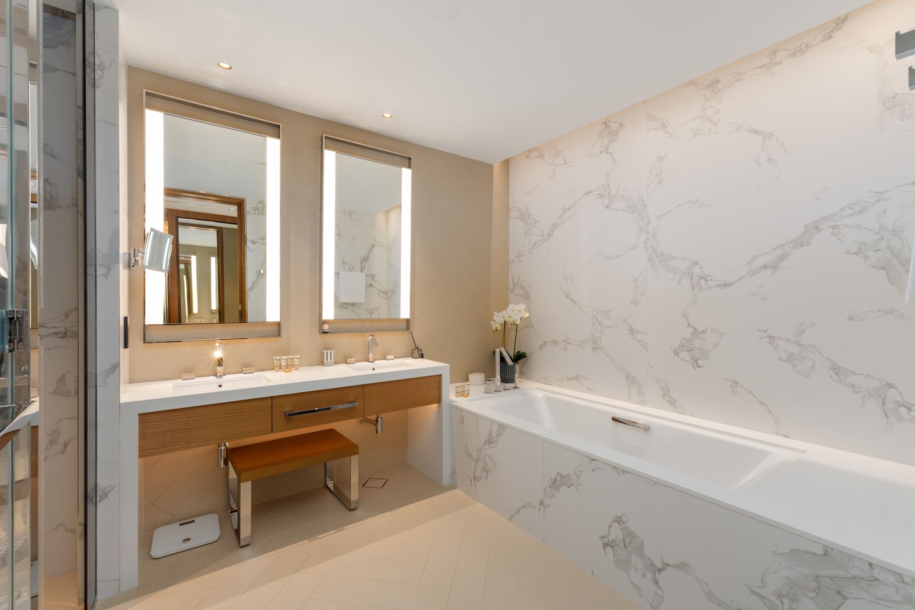 Un baño moderno con un espejo grande, una bañera y paredes con diseño de mármol.