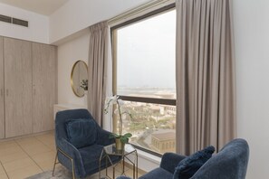 Ein modernes Wohnzimmer mit großem Fenster, einer Couch, einem Sessel und einem kleinen Tisch mit einer Pflanze.