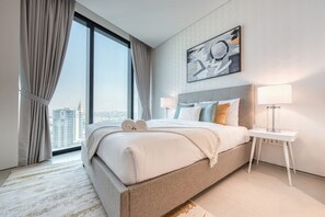 Ein modernes Hotelzimmer mit einem großen Bett, zwei Nachttischen, Blick auf die Stadt und einem Bild an der Wand.