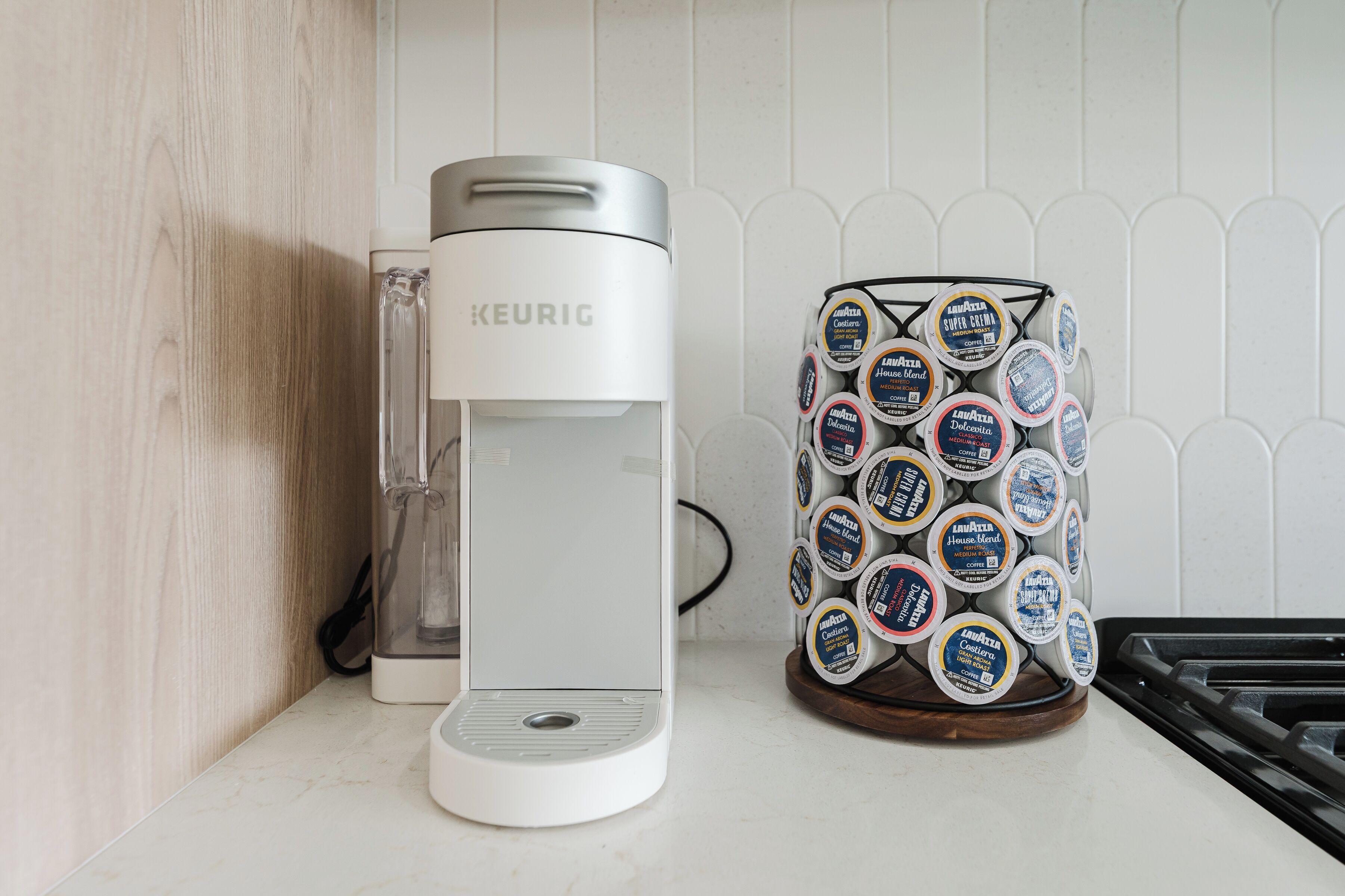 A white Keurig coffee machine and a stack of coffee pods on a kitchen counter.