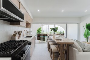 A modern kitchen with a gas stove, wooden cabinets, and a dining area with a table and chairs. - The Palmetto: Boca Pool Suite + Beach (Boca Raton)
