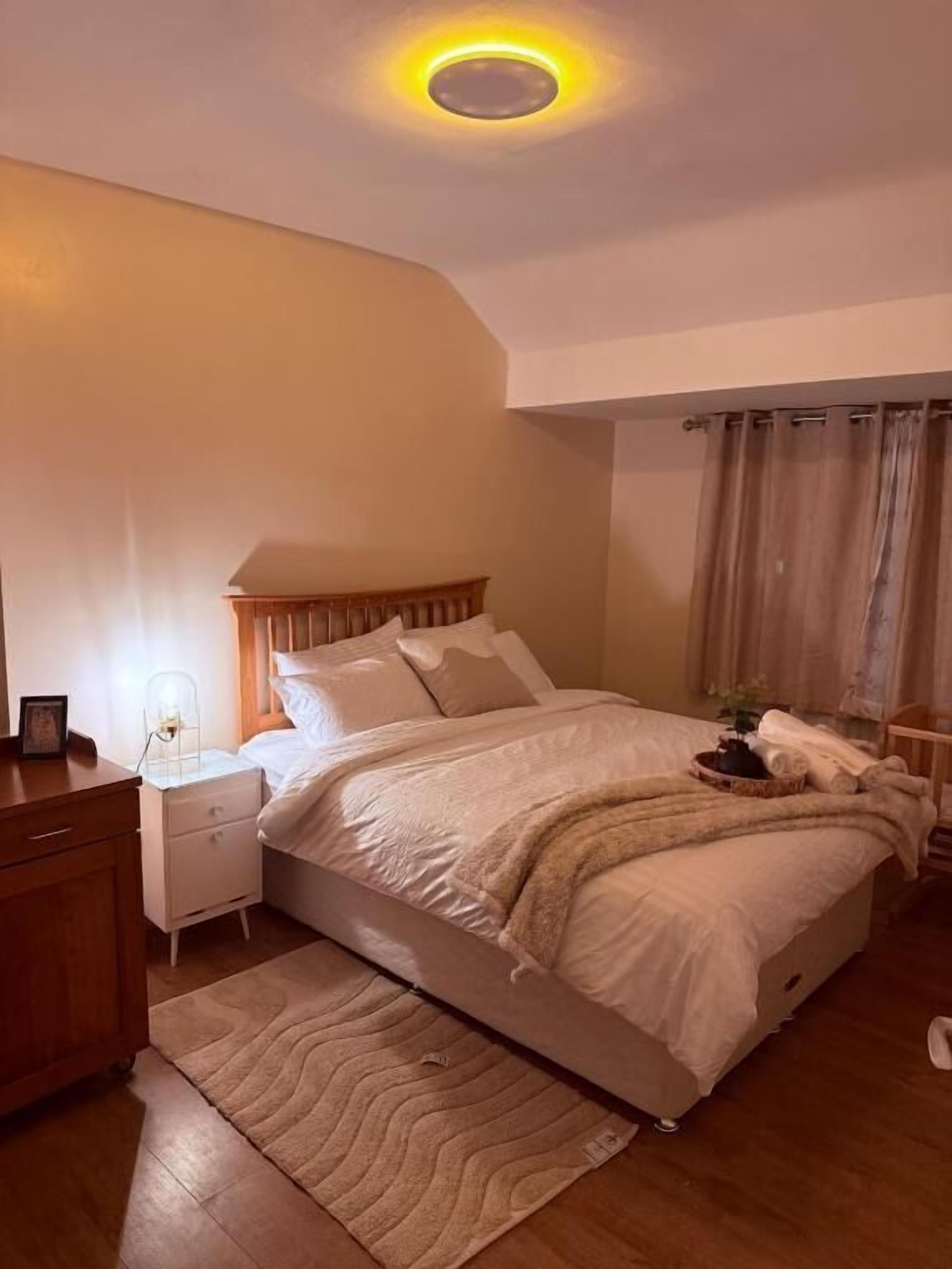 Een slaapkamer met een bed, nachtkastje, bedtafel en een plafondlamp.