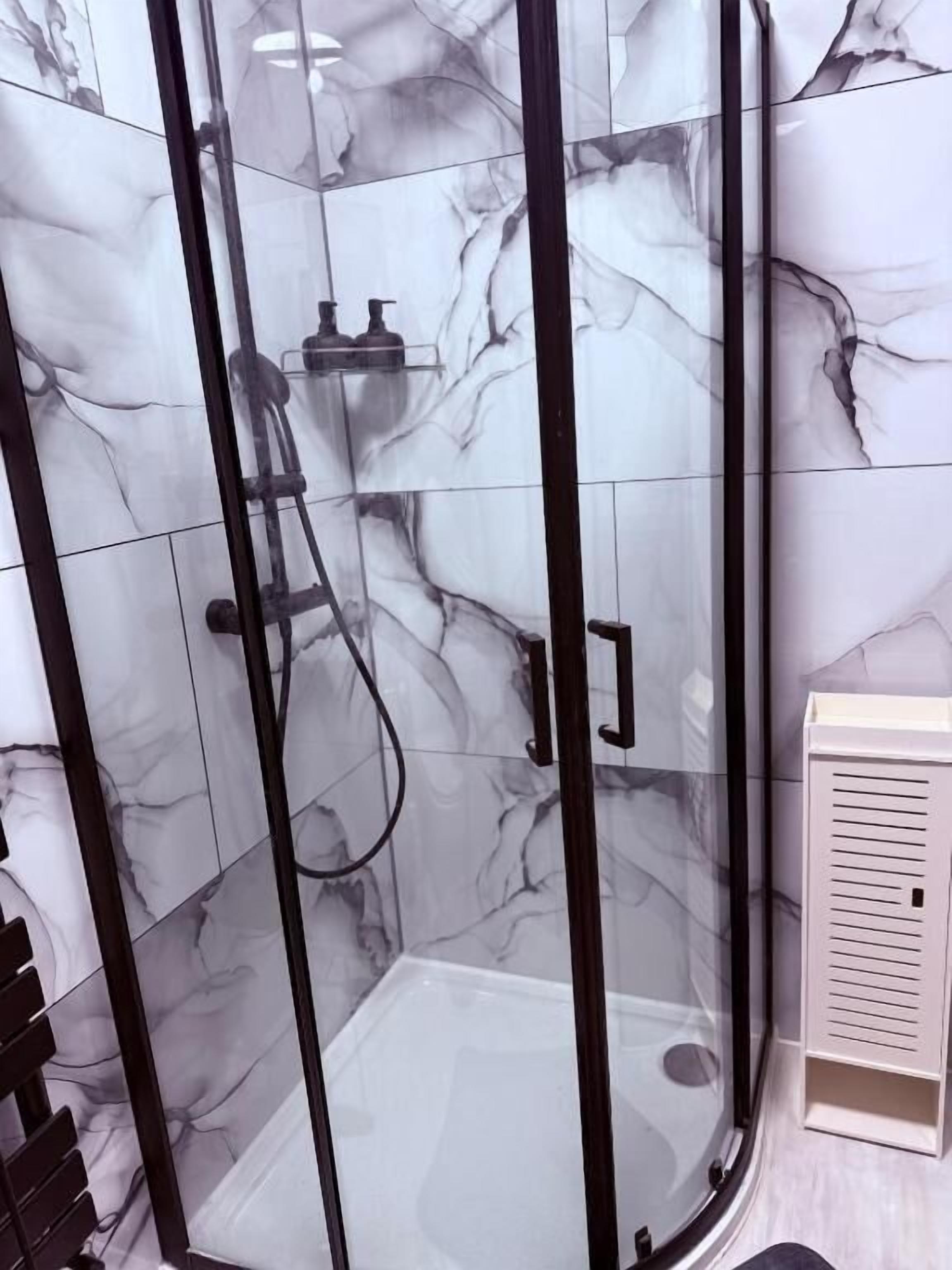 A glass-enclosed shower with a marble wall, a white sink, and a beige cabinet.