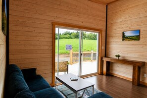 Et træinteriør med en skydedør af glas, der fører til et udendørs område, en sofa, et bord og en pejs.