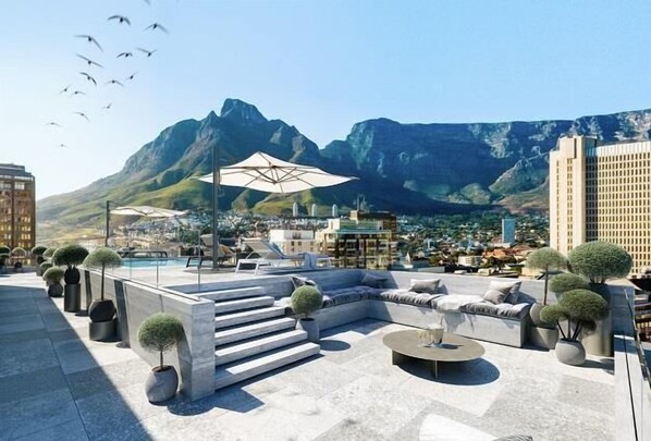 A rooftop terrace with outdoor seating, potted plants, and a view of mountains.
