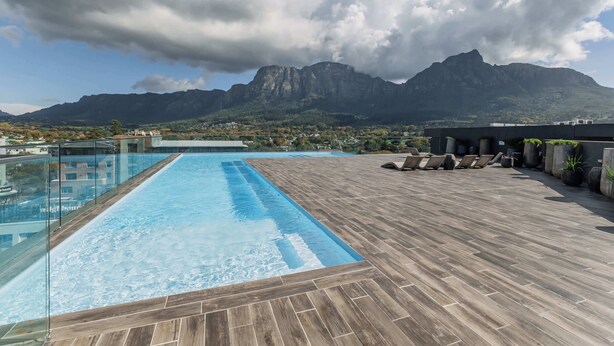 A rooftop pool with a view of mountains, wooden deck, and lounge chairs.