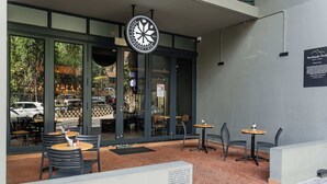An outdoor seating area with tables and chairs, a large window, and a sign for a cafe.