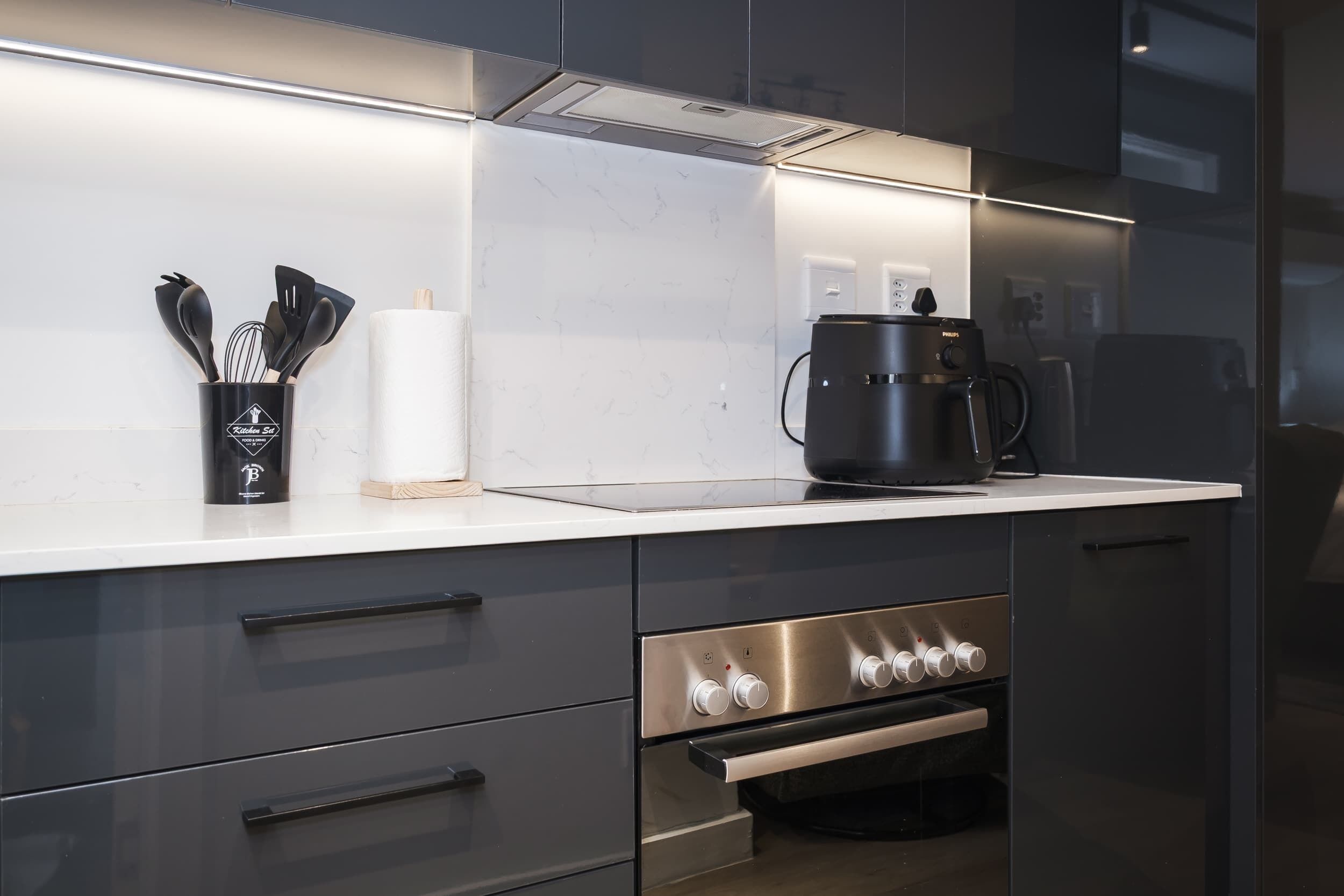 Eine moderne Küche mit einer Edelstahl-Dunstabzugshaube, einer Kaffeemaschine und einem Set schwarzer Küchenutensilien.