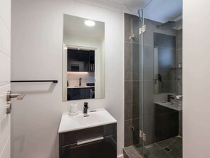 A modern bathroom with a white sink, a mirror, and a glass shower enclosure.