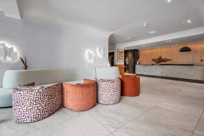 A modern reception area with a white sofa, patterned ottomans, and a reception desk.