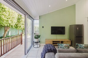 A modern living room with a flat-screen TV, a wooden entertainment unit, and a sofa. - Bishopscourt- Secret Garden hideaway (Cape Town)