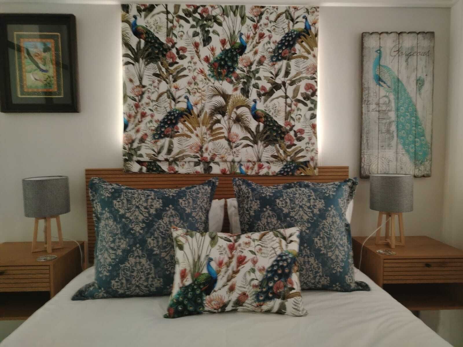 Et soveværelse med en seng, to sengeborde, en lampe på hver, og en væg med et påfuglmaleri.