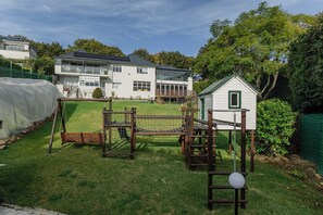 A residential area with a playground, a small shed, and a house with a balcony. - Bishopscourt- Secret Garden hideaway (Cape Town)