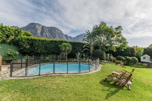 A swimming pool with a fenced deck, surrounded by a well-maintained lawn and various plants. - Bishopscourt- Secret Garden hideaway (Cape Town)