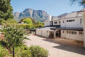 A modern house with a covered patio, a garden with tropical plants, and a mountain view in the background. - Bishopscourt- Secret Garden hideaway (Cape Town)