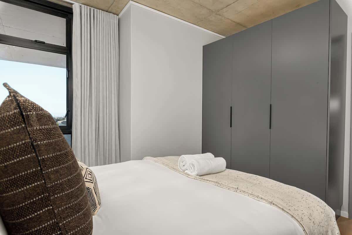 Een hotelkamer met een bed, een groot raam, een kledingkast en uitzicht op zee.