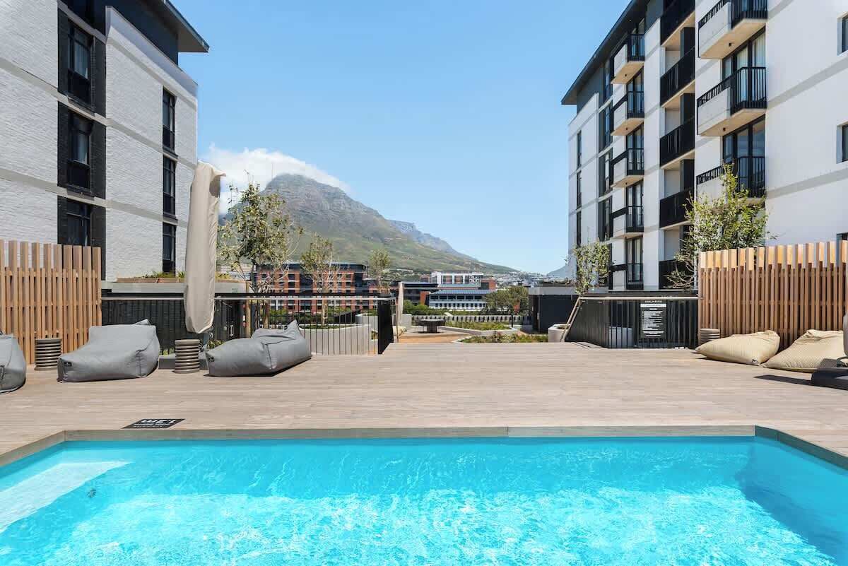 Un espace piscine offrant une vue sur une montagne, des bâtiments modernes et des espaces de détente en plein air.