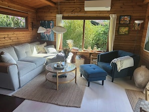 A cozy cabin interior with a sofa, ottoman, and a round table with a vase. - Log cabin within walking distance of the beach (Dronningmølle)