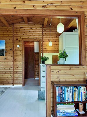 A wooden interior with a bookshelf, a door, and a hanging light fixture. - Log cabin within walking distance of the beach (Dronningmølle)