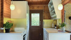 A narrow kitchen with wooden ceiling beams, white cabinetry, and pendant lights.