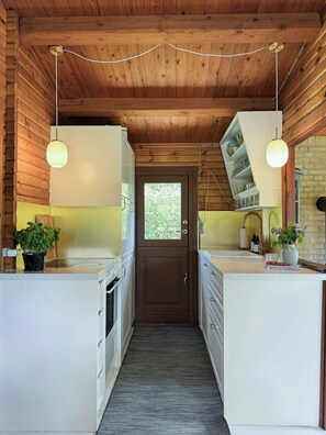 A narrow kitchen with wooden ceiling beams, white cabinetry, and pendant lights. - Log cabin within walking distance of the beach (Dronningmølle)