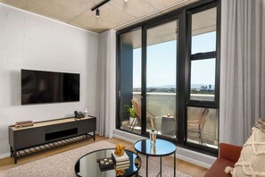 Ein modernes Wohnzimmer mit großem Fernseher, einem Glastisch, einer Couch und einem Balkon mit Aussicht.
