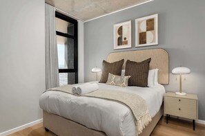 Ein modernes Schlafzimmer mit einem großen Bett, einem Nachttisch und zwei gerahmten abstrakten Kunstwerken an der Wand.