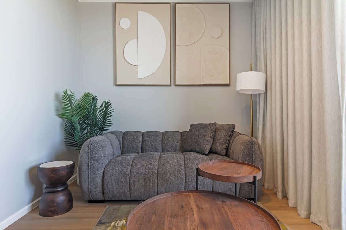 A modern living room with a gray sofa, two wooden side tables, a floor lamp, and abstract wall art.